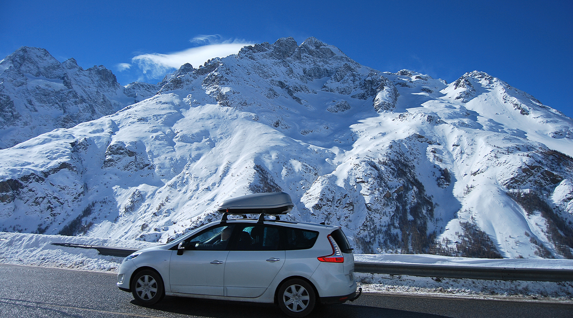silver car driving up a snowy road with mountains in the distance